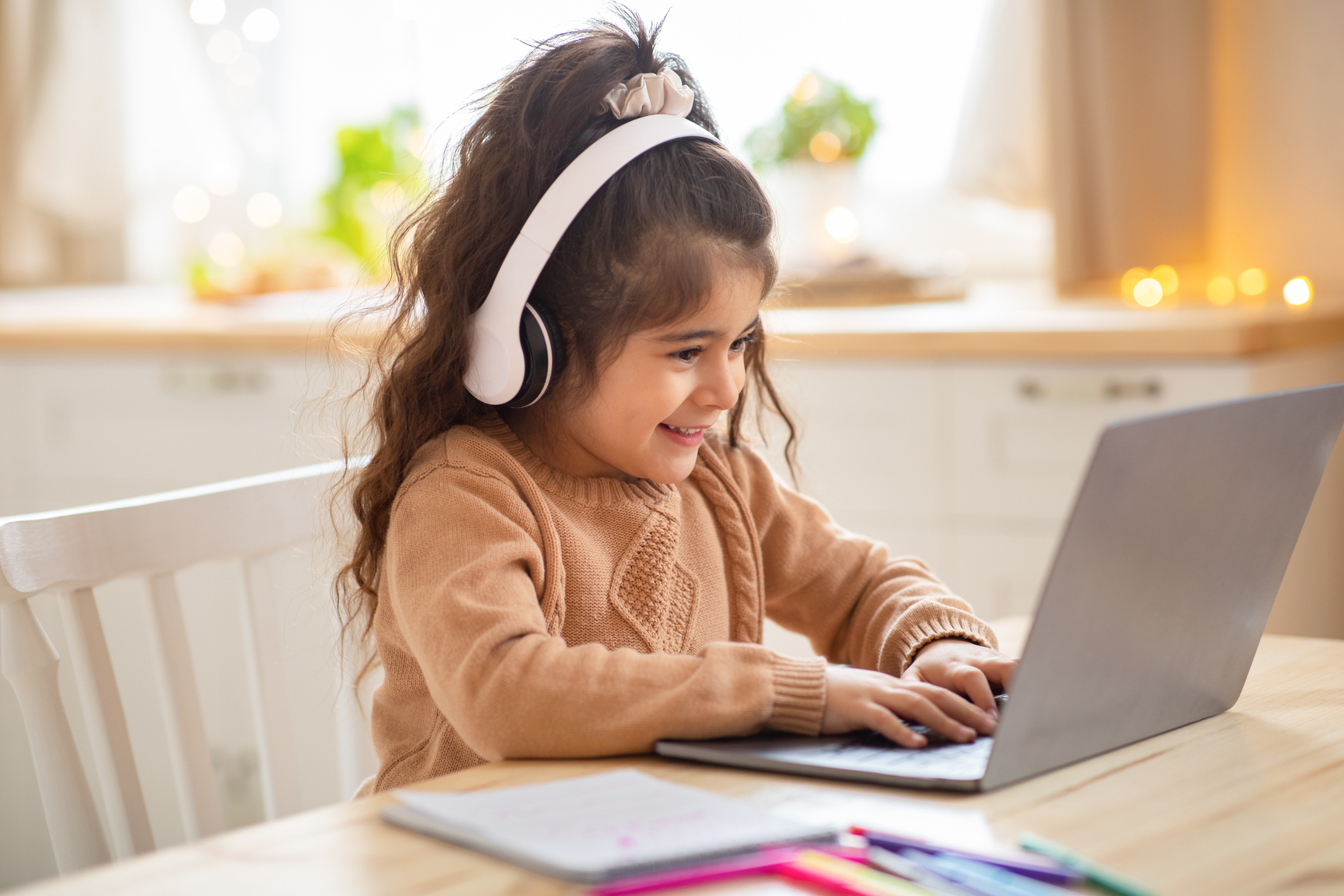 A little girl wearing headphones is using a laptop at home.